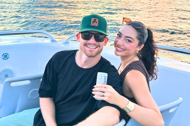Smiling couple sitting on a boat at sunset, holding a drink.