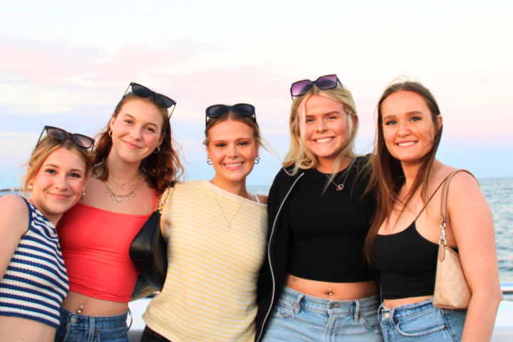 Five smiling people posing on a boat with the sea and sunset in the background.
