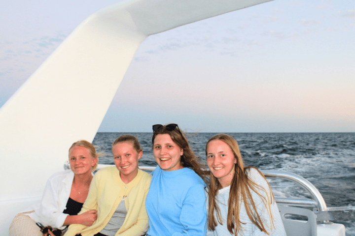 Four women sitting on a boat with ocean background.