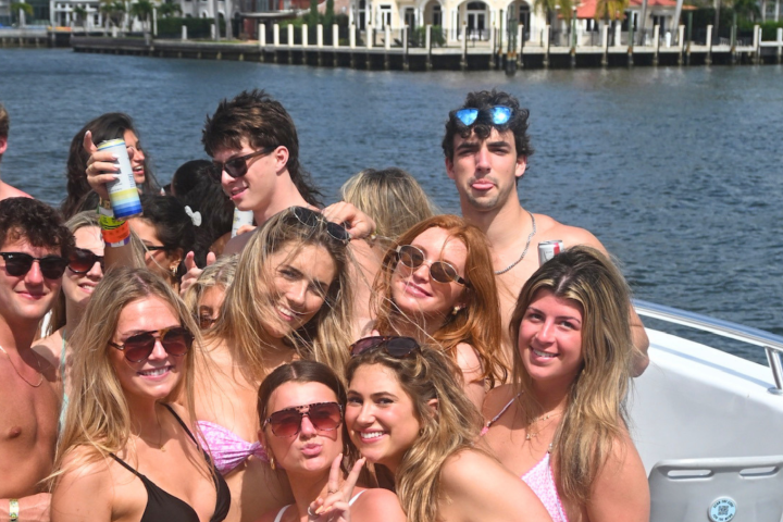 Group of smiling young adults in swimwear on a boat by the water.