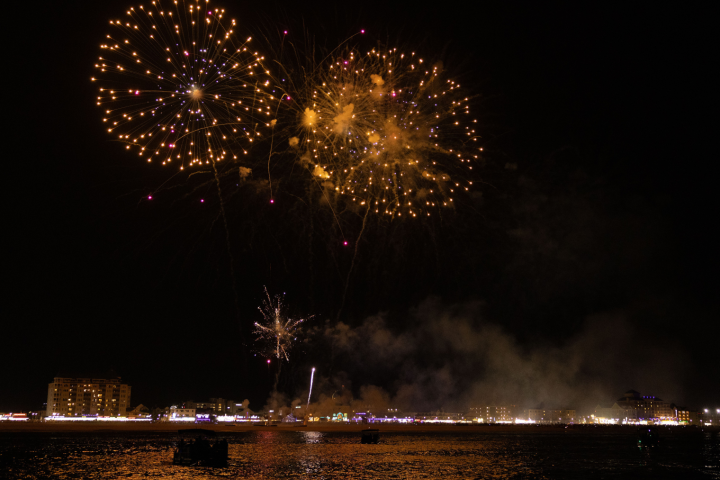 Fireworks exploding over a cityscape with water reflections at night.