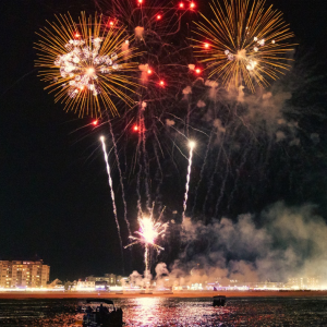 Fireworks over a cityscape at night, reflecting on water.