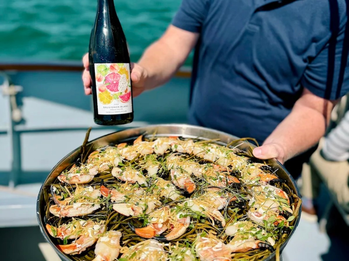 Person holding a seafood platter and wine bottle on a boat.