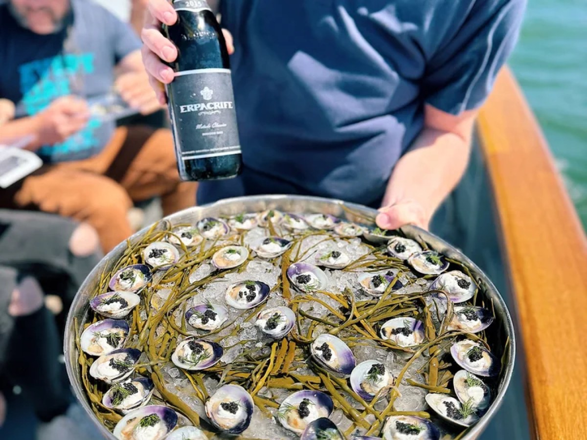Person holding tray of oysters and a bottle on a boat.