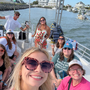 Group of people smiling on a boat in a coastal area with houses.