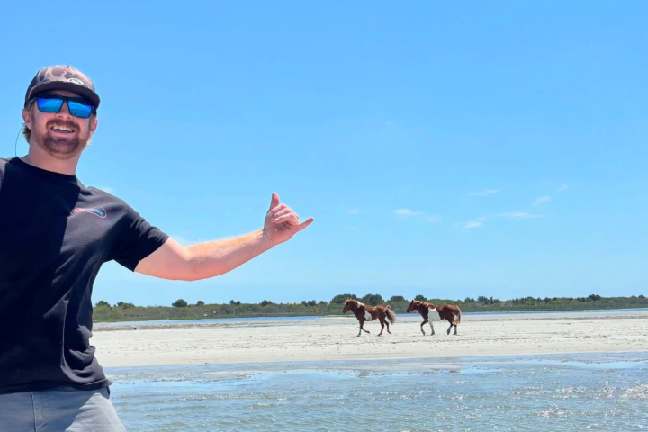 Man smiling on beach, with two horses in the background.