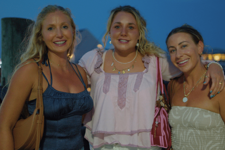 Three women smiling and posing together outdoors in evening light.