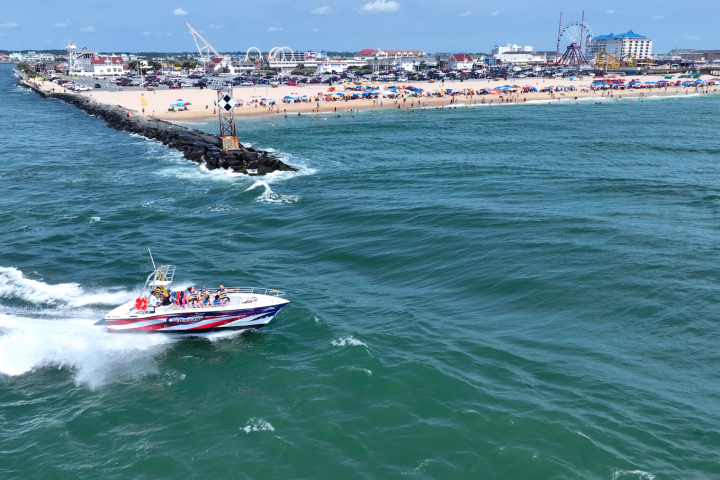 Speedboat with passengers near a beach and pier on a sunny day.