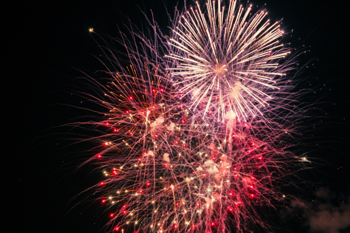 Bright fireworks exploding in the night sky with red and white bursts.